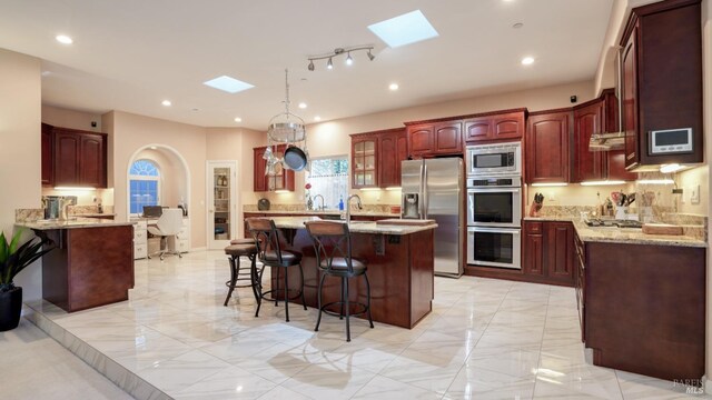 kitchen featuring a kitchen bar, dark brown cabinets, stainless steel appliances, a skylight, and light stone counters