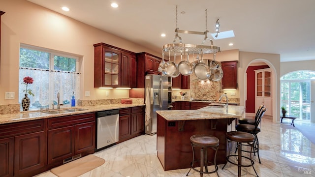 kitchen with a breakfast bar, glass insert cabinets, light stone countertops, stainless steel appliances, and a sink