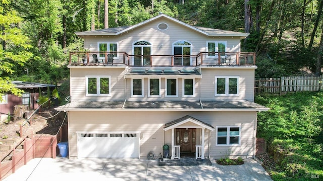 view of front of property featuring a forest view, fence, a balcony, an attached garage, and concrete driveway