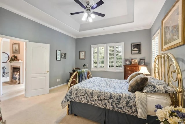 bedroom featuring ceiling fan, a glass covered fireplace, light carpet, a raised ceiling, and baseboards