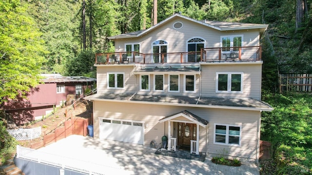 view of front of house with a forest view, fence, a balcony, an attached garage, and concrete driveway