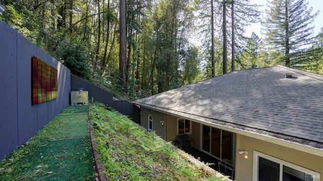 view of side of property with roof with shingles and fence