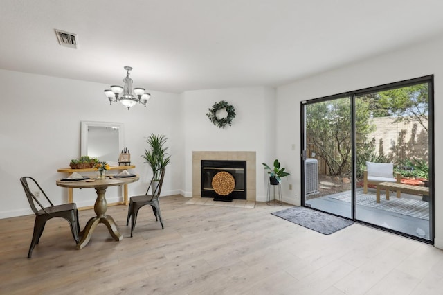 sitting room featuring a tiled fireplace, baseboards, a chandelier, and light wood-style flooring