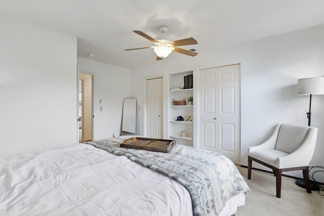bedroom featuring ceiling fan, light carpet, and multiple closets