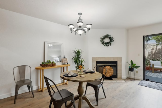 dining area with a tiled fireplace, baseboards, a notable chandelier, and light wood-style flooring