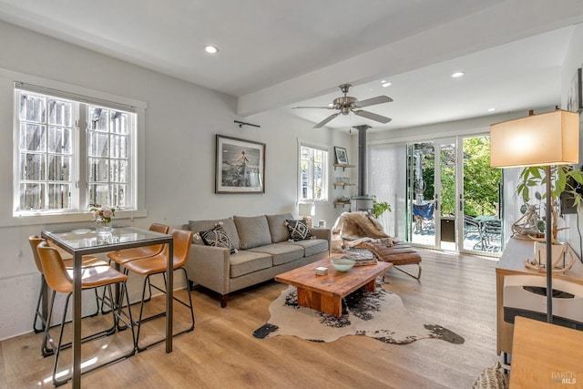 living area with a wood stove, light wood-type flooring, beam ceiling, recessed lighting, and ceiling fan