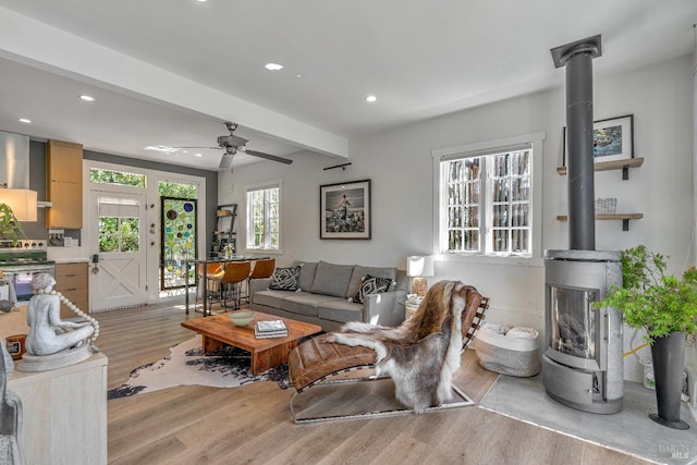 living room featuring a wood stove, light wood-style floors, recessed lighting, beamed ceiling, and ceiling fan