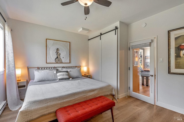 bedroom featuring a barn door, light wood-style floors, a baseboard heating unit, baseboards, and a ceiling fan