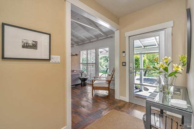 doorway with beam ceiling, wood-type flooring, and baseboards