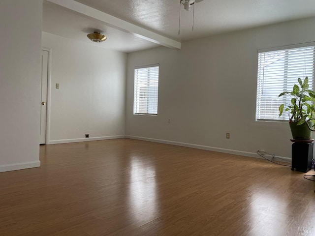 empty room with beamed ceiling, ceiling fan, wood finished floors, and baseboards