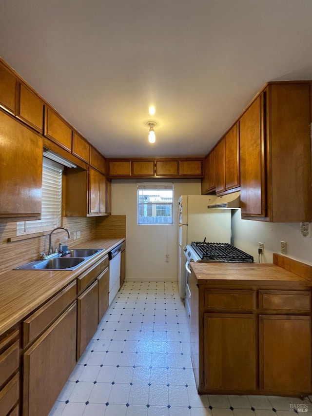 kitchen with tasteful backsplash, light floors, under cabinet range hood, brown cabinets, and a sink