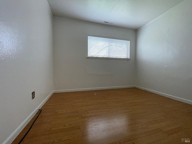 spare room featuring wood finished floors, visible vents, crown molding, and baseboards