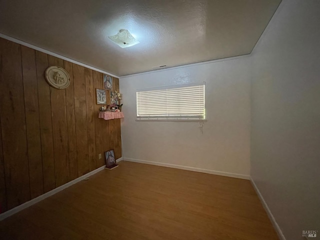 empty room with wood walls, wood finished floors, and baseboards
