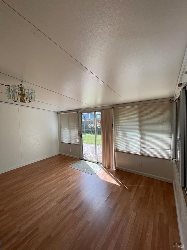 spare room with an inviting chandelier, a textured ceiling, wood finished floors, and baseboards