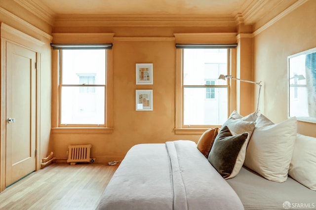 bedroom featuring multiple windows, crown molding, radiator, and wood finished floors