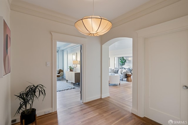 hall featuring baseboards, arched walkways, and light wood-style floors