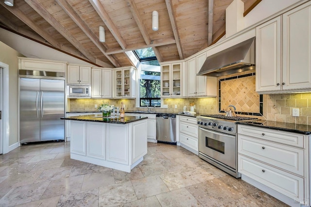 kitchen featuring tasteful backsplash, built in appliances, vaulted ceiling with skylight, a kitchen island, and ventilation hood
