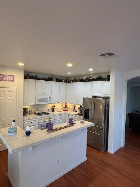 kitchen featuring visible vents, arched walkways, high quality fridge, white microwave, and dark wood-type flooring