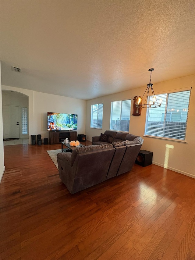 living area featuring an inviting chandelier, arched walkways, a textured ceiling, visible vents, and wood finished floors