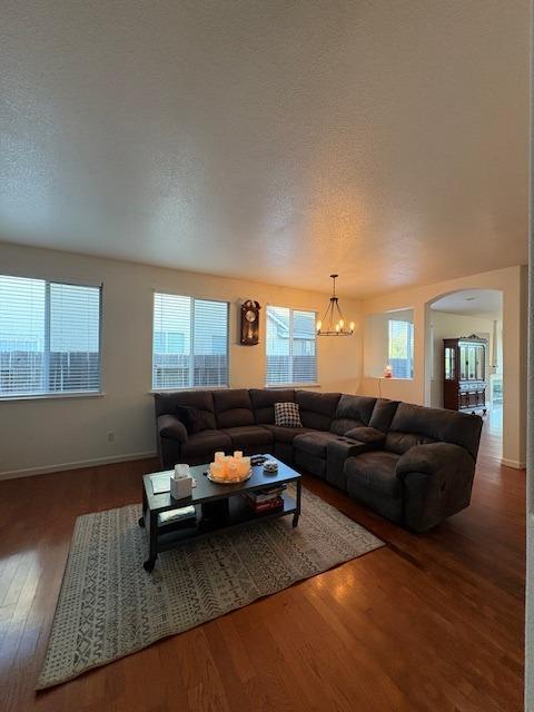 living room featuring arched walkways, a textured ceiling, an inviting chandelier, and wood finished floors