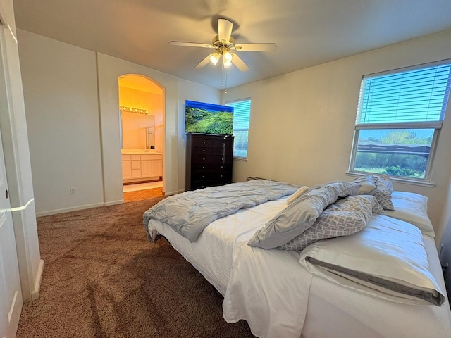 carpeted bedroom featuring arched walkways, ensuite bathroom, multiple windows, and baseboards