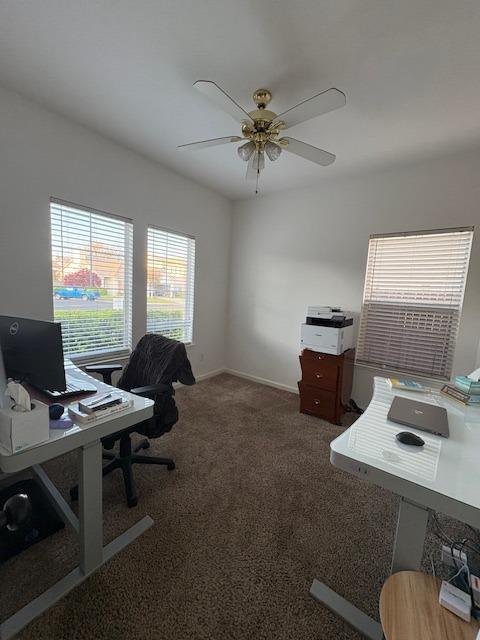 carpeted office space with baseboards and a ceiling fan