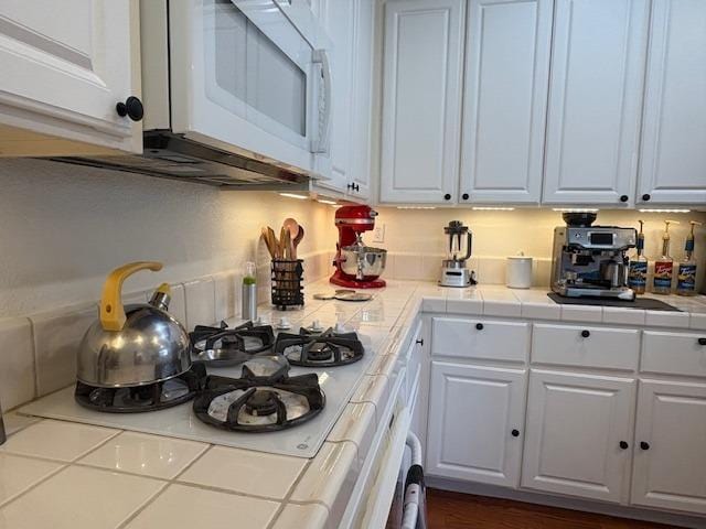 kitchen featuring white microwave, tile countertops, and white cabinets