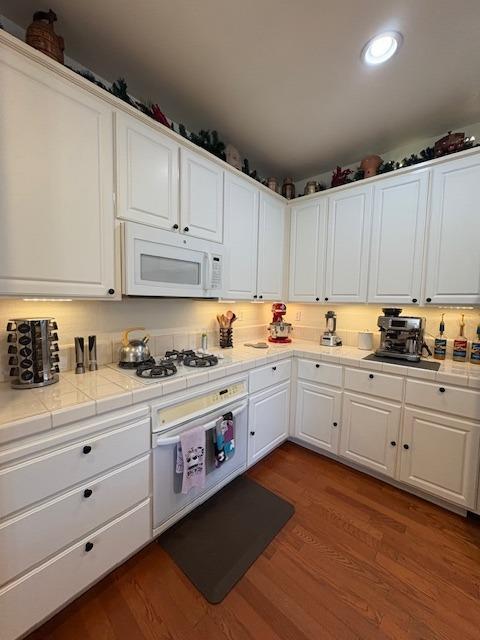kitchen with white cabinets, white appliances, dark wood-style floors, and tile counters