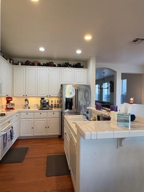 kitchen with a sink, white cabinetry, tile countertops, and wood finished floors