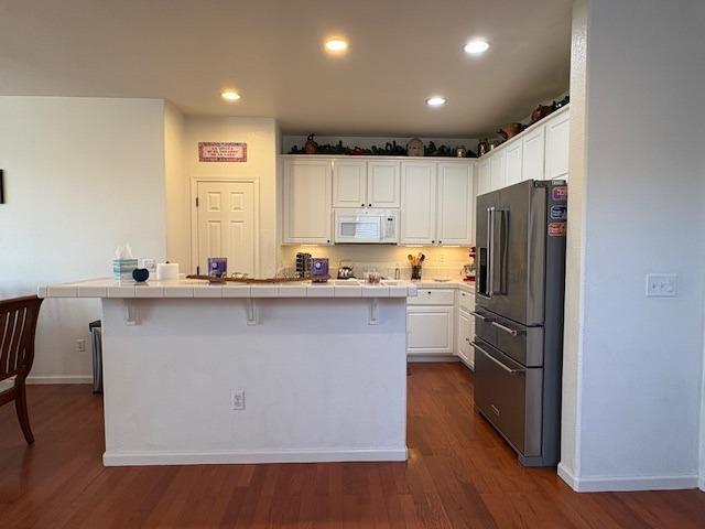 kitchen featuring baseboards, high end fridge, white microwave, white cabinetry, and tile countertops