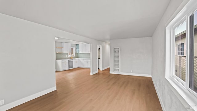unfurnished living room with baseboards, a sink, and light wood-style flooring