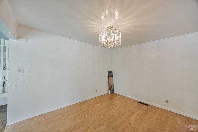 empty room with baseboards, light wood finished floors, a chandelier, and visible vents