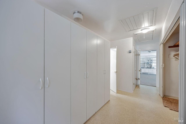 hall featuring attic access, baseboards, visible vents, and light speckled floor