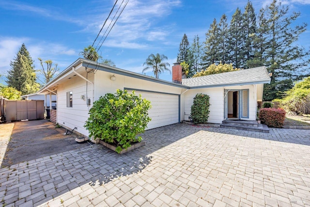 view of front of home with an attached garage, a chimney, and fence