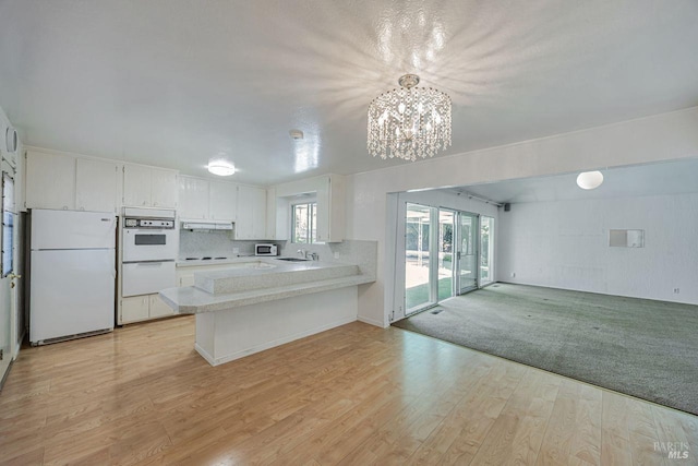 kitchen featuring under cabinet range hood, an inviting chandelier, light countertops, white appliances, and open floor plan