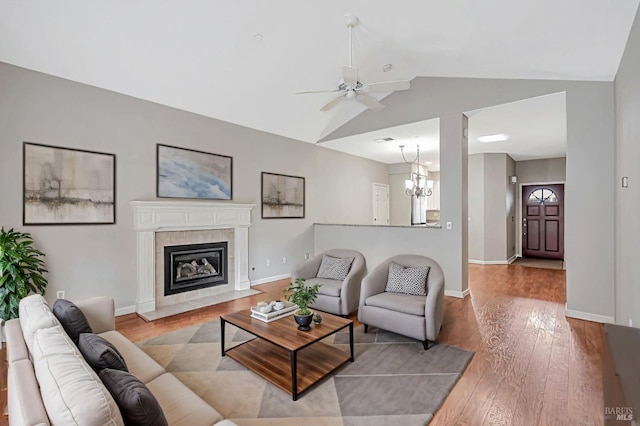 living room with ceiling fan with notable chandelier, a fireplace, wood finished floors, lofted ceiling, and baseboards