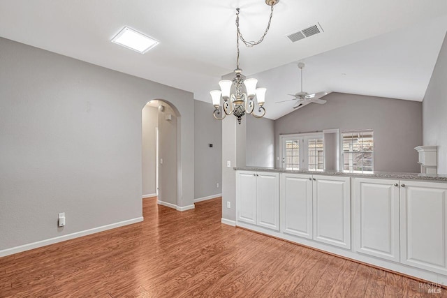 empty room featuring arched walkways, light wood finished floors, visible vents, and ceiling fan with notable chandelier