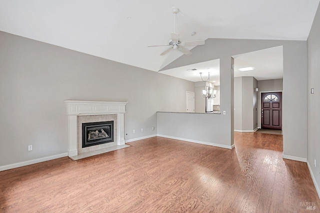 unfurnished living room with baseboards, a tiled fireplace, ceiling fan with notable chandelier, wood finished floors, and vaulted ceiling