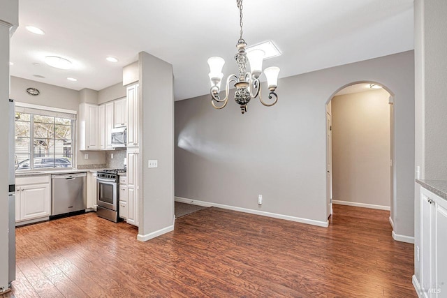 kitchen with baseboards, white cabinetry, appliances with stainless steel finishes, arched walkways, and wood finished floors