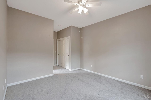 spare room featuring light colored carpet, ceiling fan, and baseboards