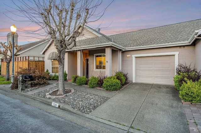 view of front facade with an attached garage, fence, a shingled roof, and stucco siding