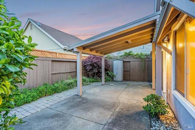 patio terrace at dusk featuring an outdoor structure, a fenced backyard, and a storage shed