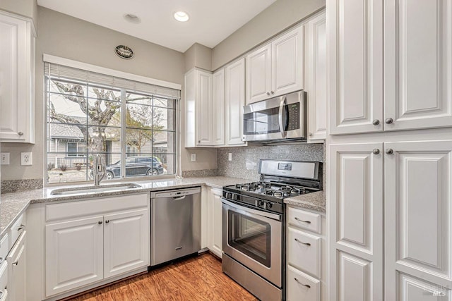 kitchen featuring a sink, appliances with stainless steel finishes, white cabinetry, backsplash, and light stone counters
