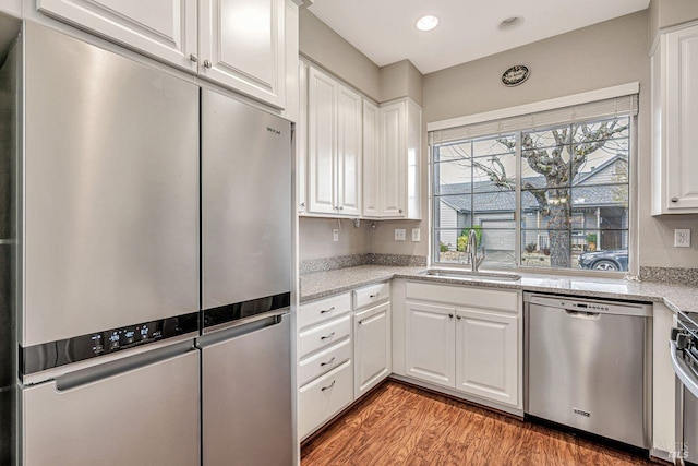 kitchen featuring light stone countertops, light wood-style flooring, white cabinetry, a sink, and stainless steel appliances