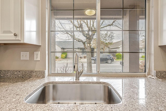 details featuring a sink, white cabinetry, a textured wall, and light stone countertops