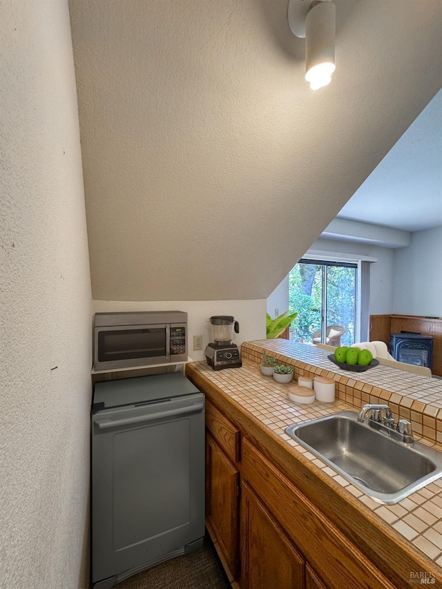kitchen featuring a sink, stainless steel microwave, fridge, vaulted ceiling, and tile countertops