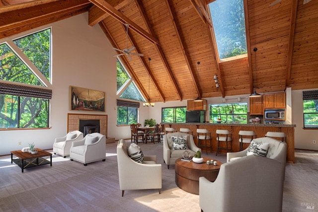 carpeted living room featuring a tiled fireplace, wood ceiling, beamed ceiling, a skylight, and high vaulted ceiling