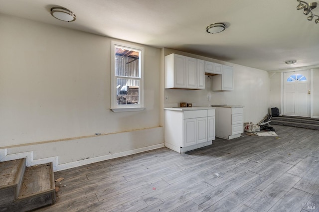 kitchen with light countertops, light wood finished floors, baseboards, and white cabinets