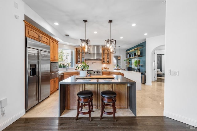 kitchen with a breakfast bar, glass insert cabinets, wall chimney exhaust hood, appliances with stainless steel finishes, and a sink