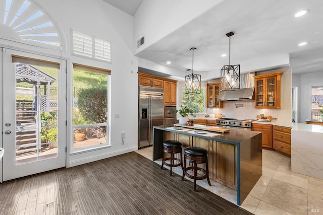 kitchen with visible vents, a center island, glass insert cabinets, under cabinet range hood, and stainless steel appliances